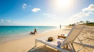 Spiaggia soleggiata con mare cristallino, una persona in riva e lettino sulla sabbia
