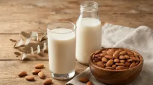 Bicchiere e bottiglia di latte di mandorla con ciotola di mandorle su tavolo di legno